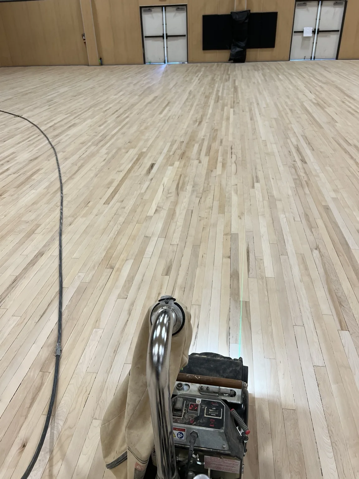 View from behind a professional hardwood floor sanding machine on a commercial gym floor